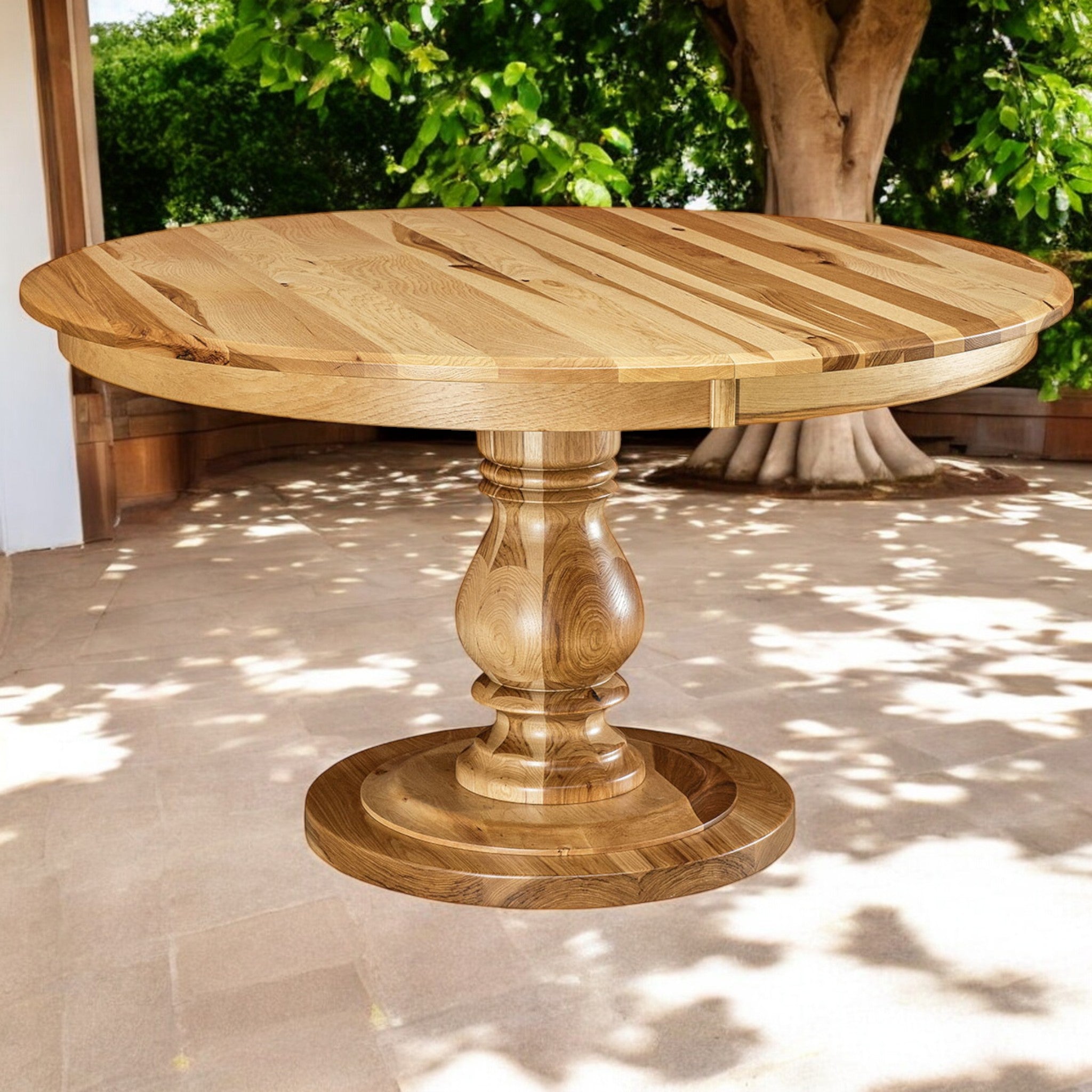 Wooden round table with a pedestal base on a patio with greenery in the background