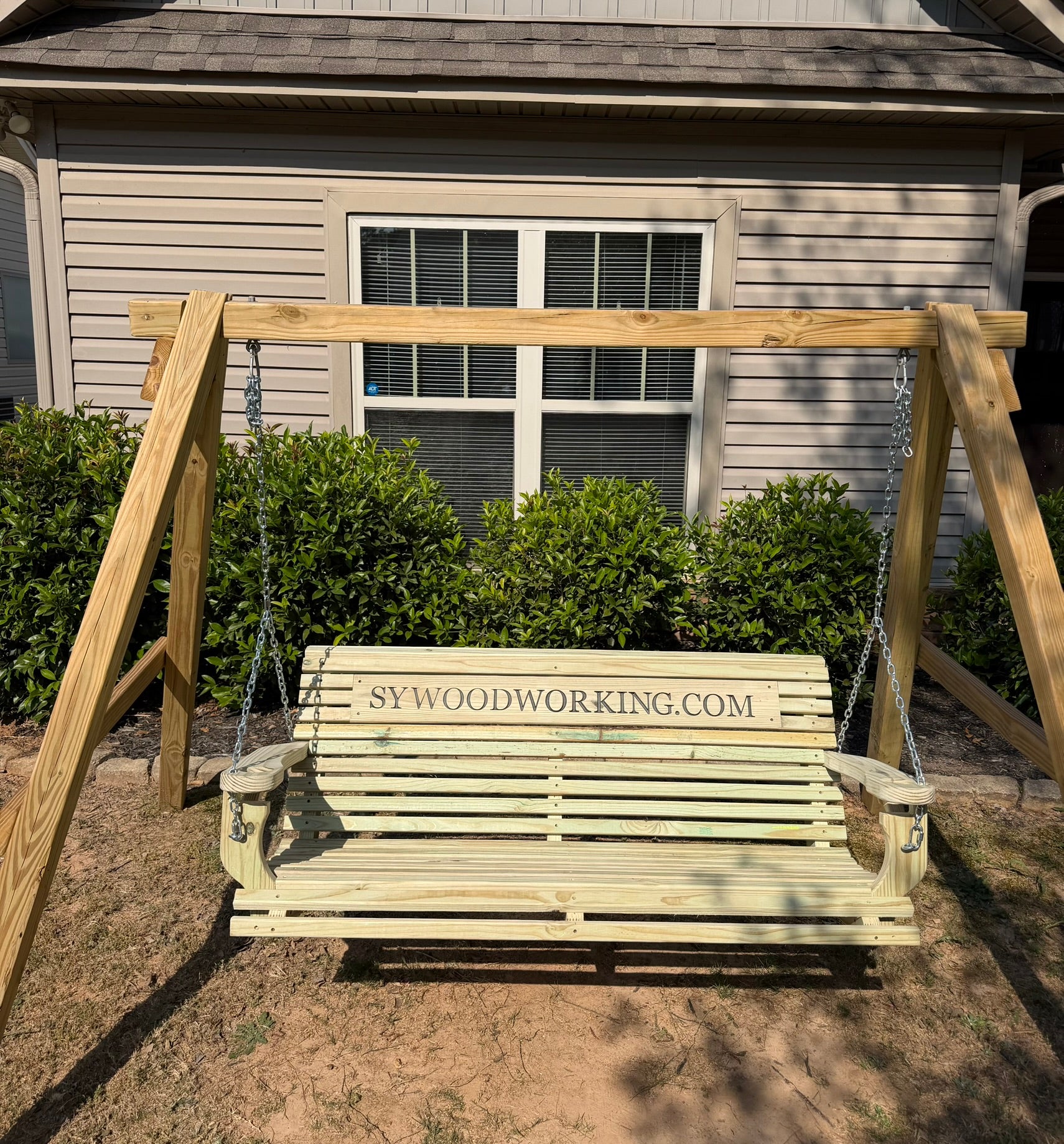 Wooden swing with 'SYWoodworking.com' branding in front of a house.