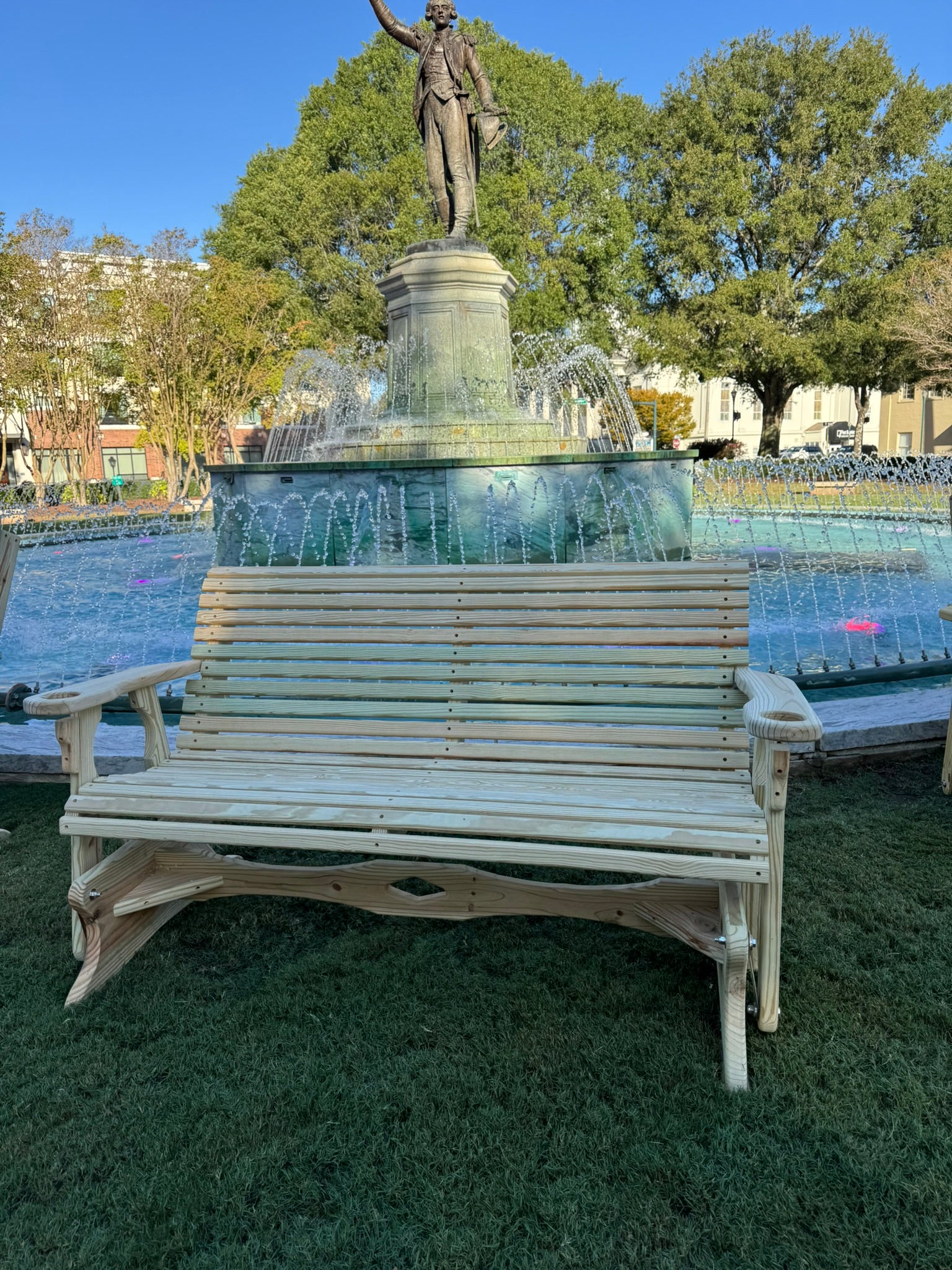 Wooden lounge chair in front of a fountain with a statue in a park setting