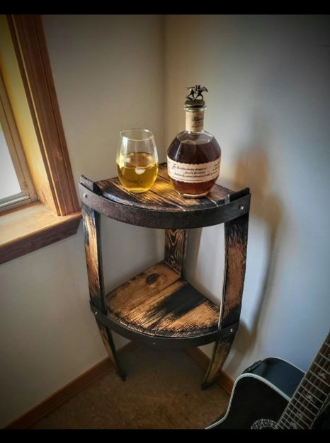Bottle of whiskey and a glass on a wooden barrel table by a window.