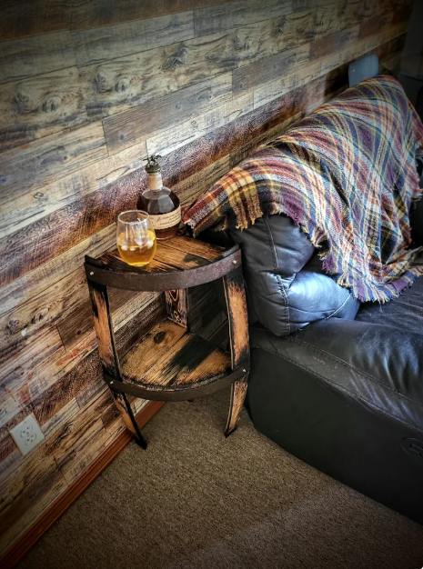 Wooden side table with a glass and bottle against a rustic wooden wall.